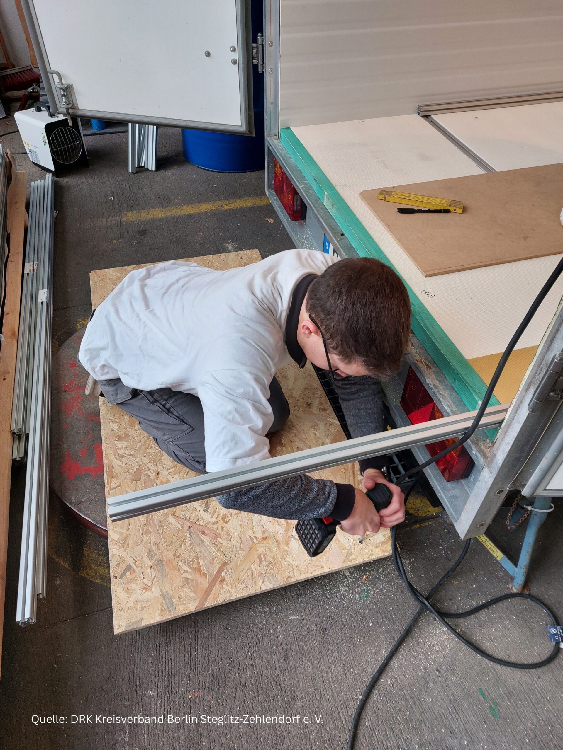 Man sieht einen Ehrenamtlichen, der eine handwerkliche Arbeit am Anhänger durchführt