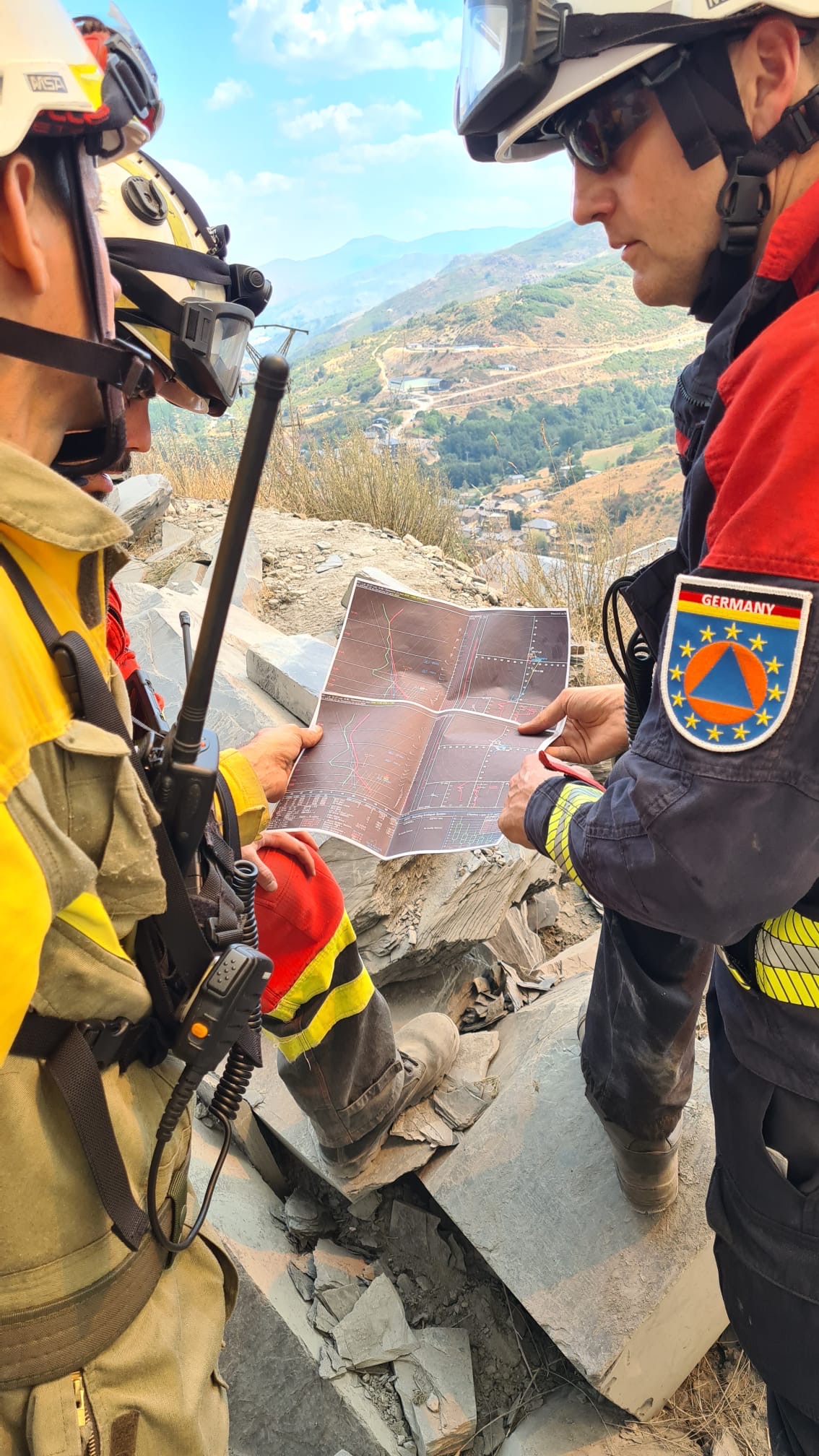 Man sieht zwei Feuerwehrmänner in Einsatzkleidung. Sie halten gemeinsam eine Lagekarte und Blicken in das Gelände.