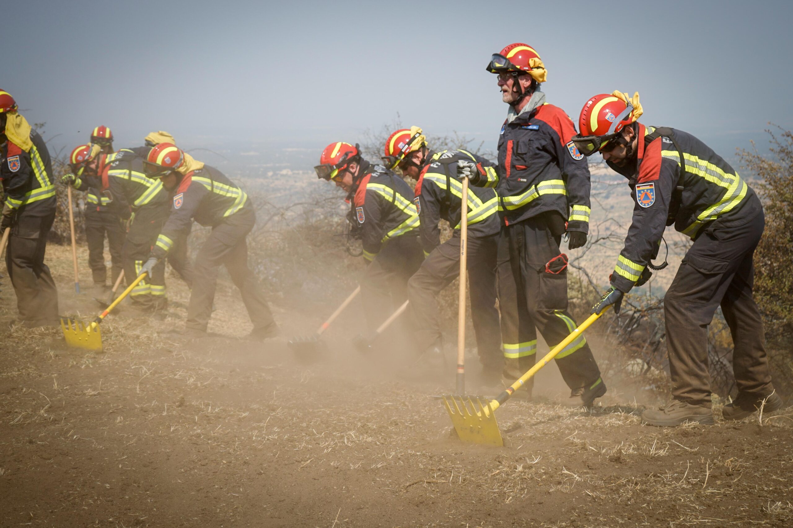 Feuerwehrleute in Einsatzkleidung mit Gerätschaften bearbeiten den trockenen Boden