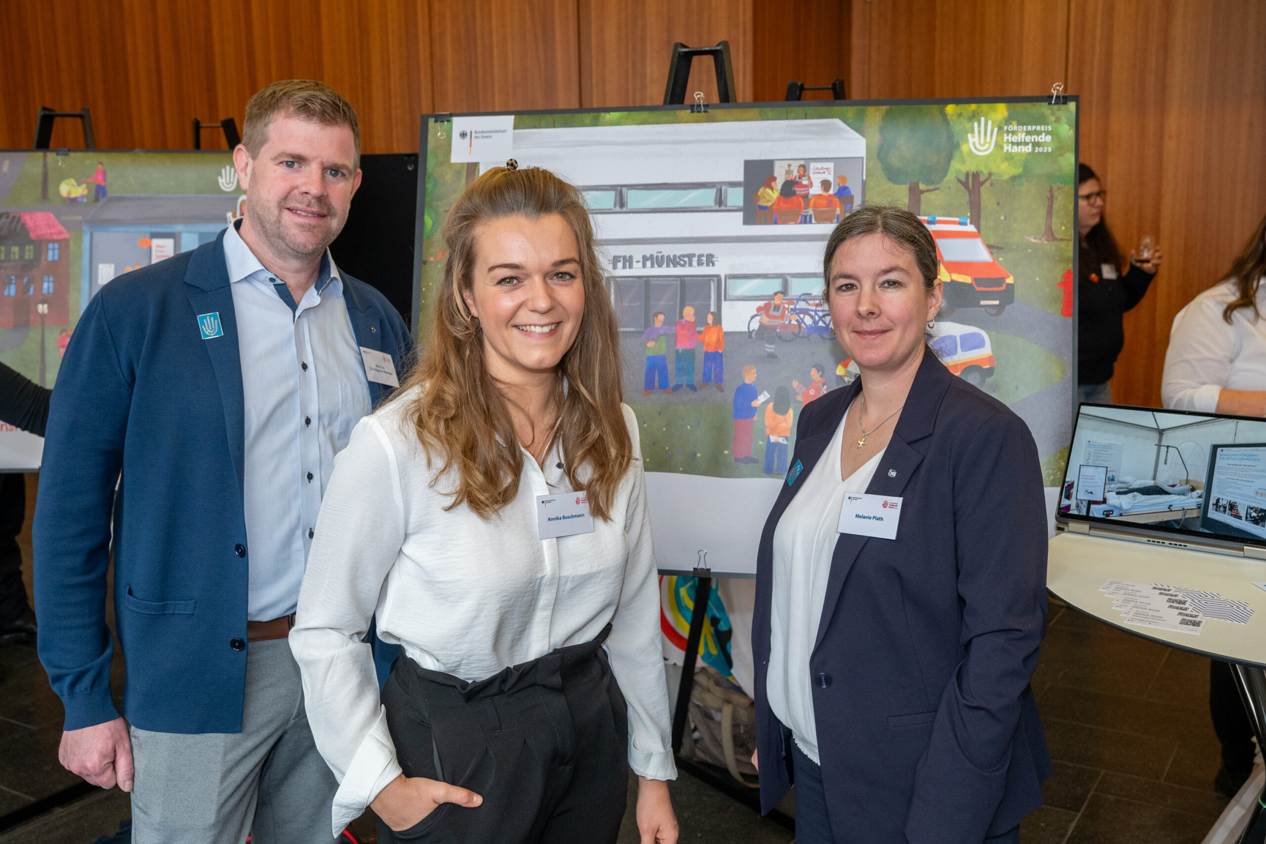 Drei Personen stehen vor einem Plakat bei einer Ausstellung.