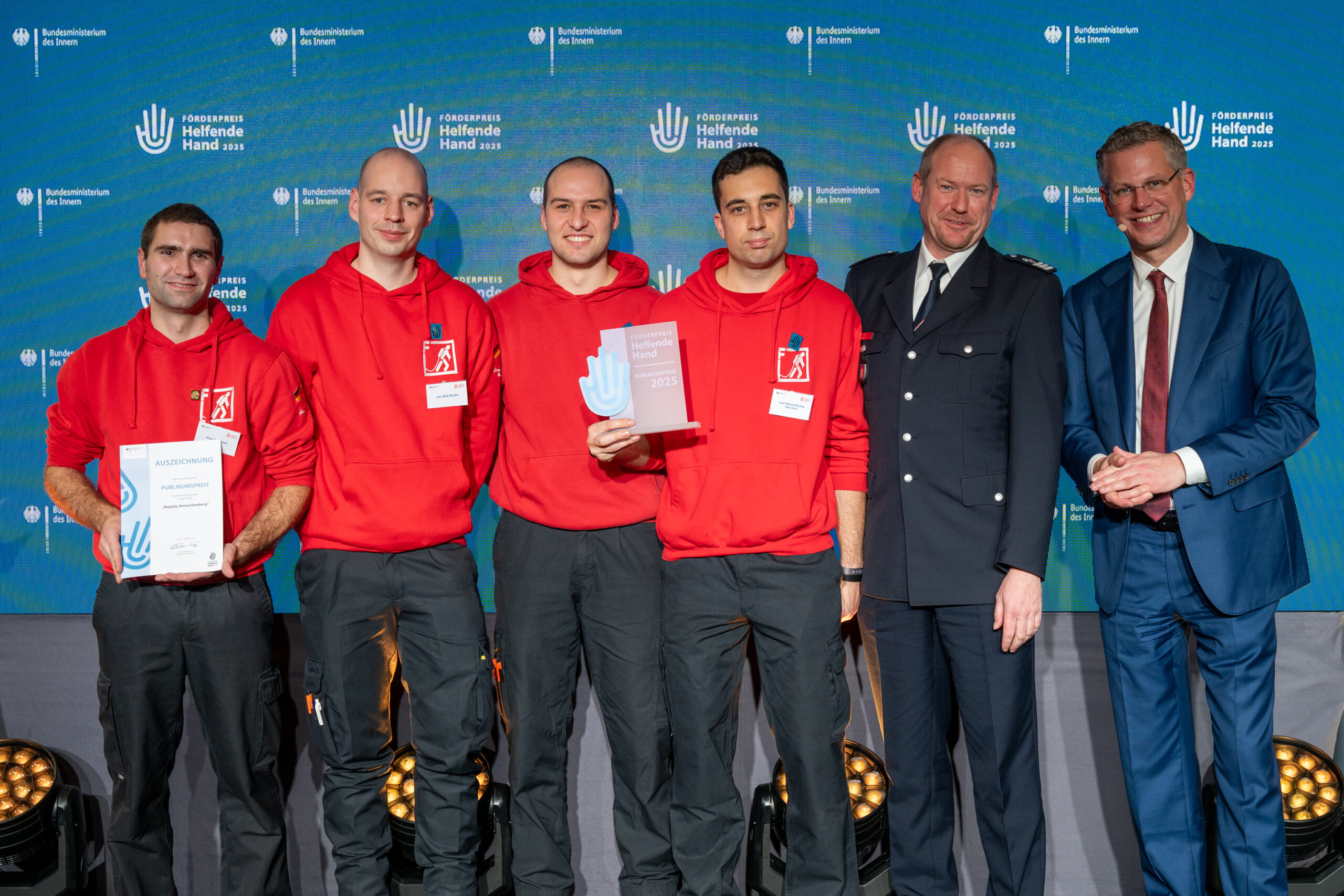Die Vertreter des TFA-Teams stehen auf der Bühne. Sie tragen rote Pullover und eine Dienstuniform.